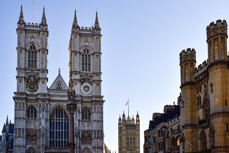 The image shows the exterior of Westminster Abbey with its Gothic architecture, including two prominent towers with pointed spires and detailed stone carvings. In the foreground, a tall, dark-colored
