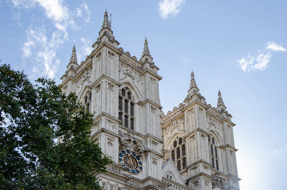 The image shows the exterior of Westminster Abbey with its Gothic architecture, including two prominent towers with pointed spires and detailed stone carvings. In the foreground, a tall, dark-colored